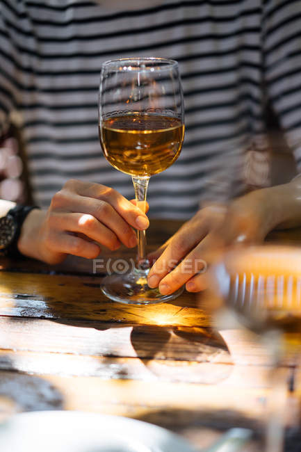 Mãos femininas segurando elegante copo de vinho branco na mesa de madeira ao ar livre — Fotografia de Stock