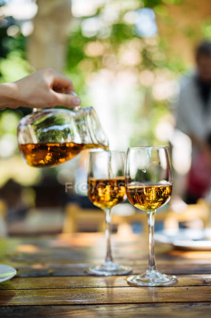 Main humaine verser du vin blanc du pichet en verre dans des verres sur la table à l'extérieur — Photo de stock