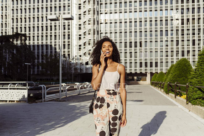 Élégante femme afro-américaine parlant sur smartphone tout en marchant sur la rue de la ville le jour ensoleillé — Photo de stock