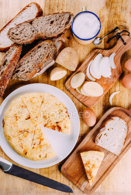 Torta de corte fresco em prato em mesa de madeira com tábuas de corte, pão e legumes fatiados — Fotografia de Stock