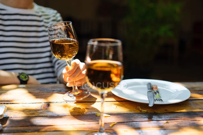 Крупный план человеческой руки с бокалом белого вина на деревянном столе на открытом воздухе — стоковое фото