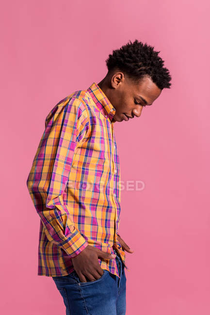 Hipster black man in colorful shirt standing on pink background and looking down — Stock Photo