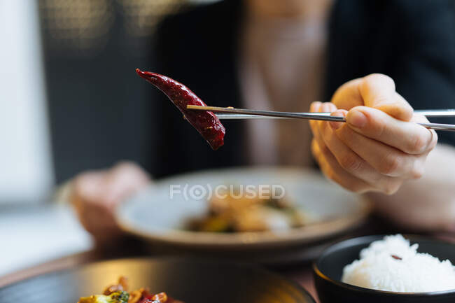 Primer plano de la mujer con palillos que muestran delicioso chile picante? pimiento rojo - foto de stock