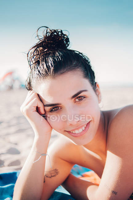 Sorridente ragazza sdraiata sulla spiaggia alla luce del sole e guardando la fotocamera — Foto stock