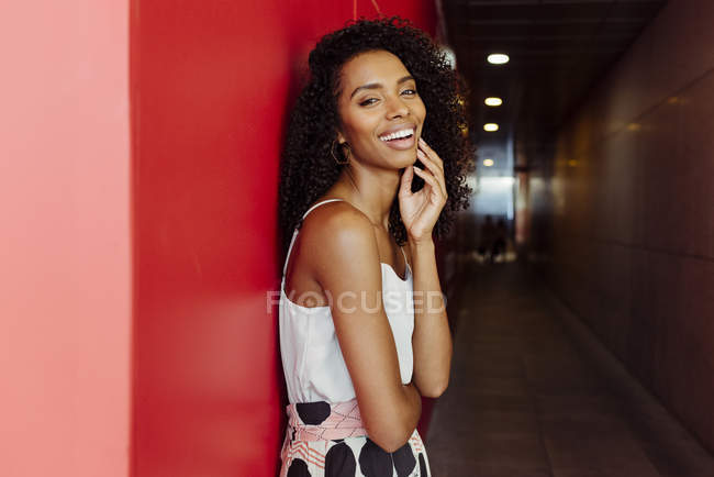 Smiling African-American woman in elegant outfit standing on red background — Stock Photo