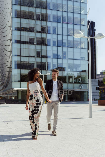 Elegantes multiethnisches Paar hält Händchen, während es in der modernen Stadt spaziert — Stockfoto