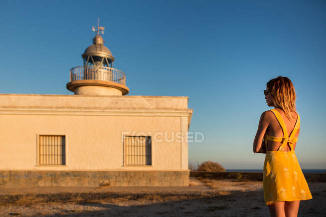 Женщина в платье, стоящая на берегу перед маяком — стоковое фото