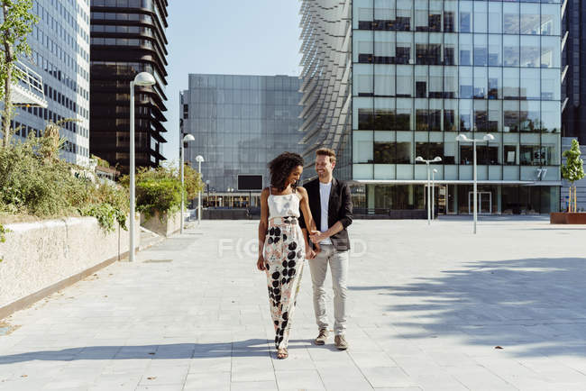 Elegant multiracial couple holding hands while walking in modern city — Stock Photo