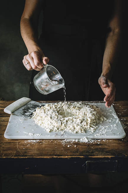 Cropped shot of woman pouring water into pile of flour and butter mixture — Stock Photo