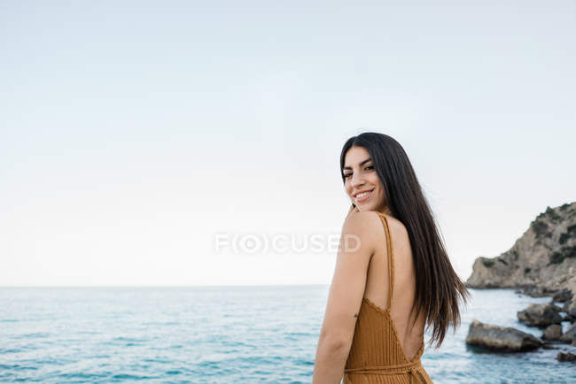 Stylish brunette looking over shoulder on rocky coast — Stock Photo