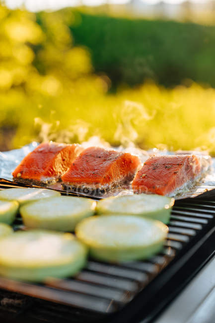 Salmon and zucchini pieces with foil on grill grid outdoors — Stock Photo
