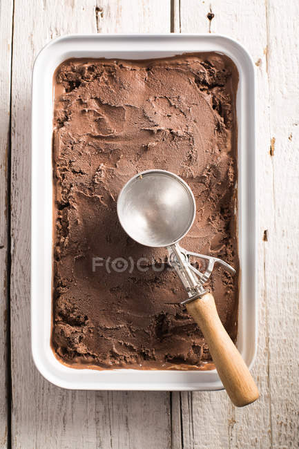 Homemade chocolate ice cream in box with scoop on wooden surface — Stock Photo