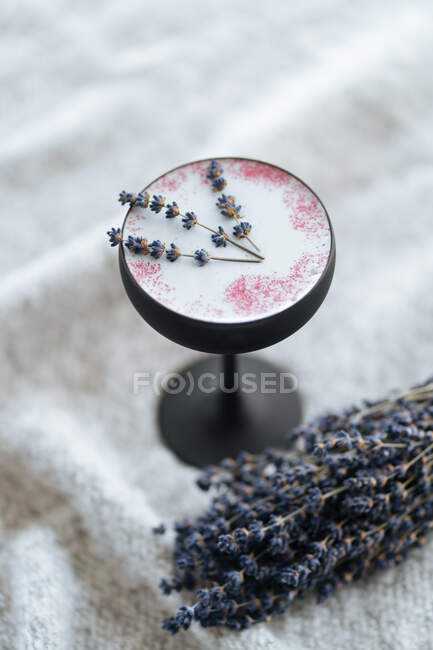 Beautiful Nordic drink in small high stem glass sprinkled with red powder and leaf served on grey cloth with scattered dried rose petals on blurred background — Stock Photo