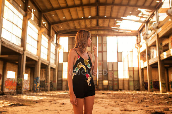 Jeune femme sans émotion debout dans un bâtiment abandonné au coucher du soleil — Photo de stock