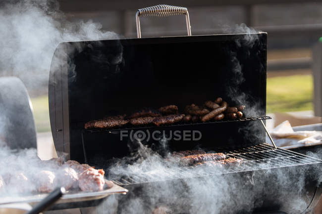 Hamburguesas crudas asando en rejilla de parrilla barbacoa al aire libre - foto de stock