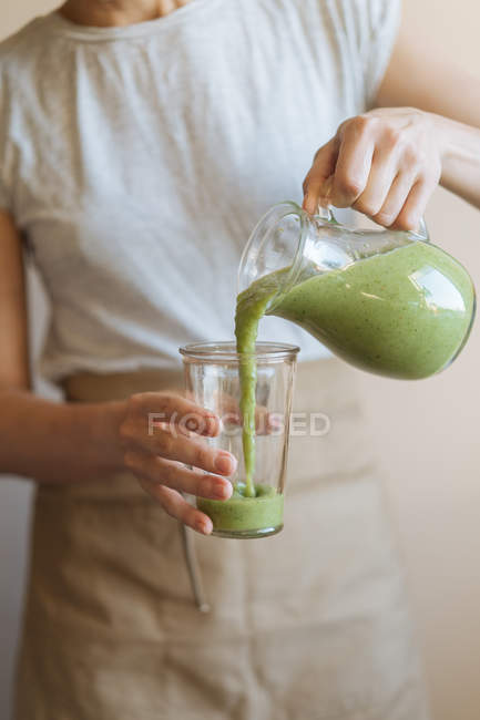 Mani femminili versando frullato verde sano dalla tazza del frullatore in vetro — Foto stock