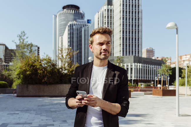 Вдумливий елегантний чоловік використовує смартфон у сучасному місті — стокове фото