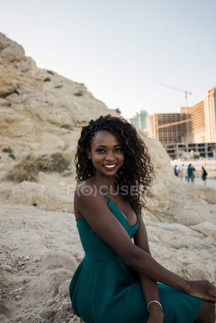 Femme noire joyeuse avec des boucles assis sur la plage de sable — Photo de stock