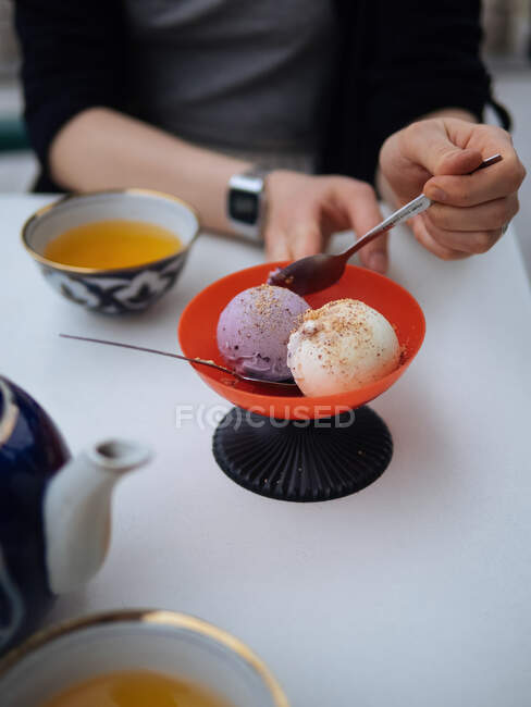 Vista da colheita da pessoa sem rosto sentada à mesa com chá e colher de espera com sorvete — Fotografia de Stock