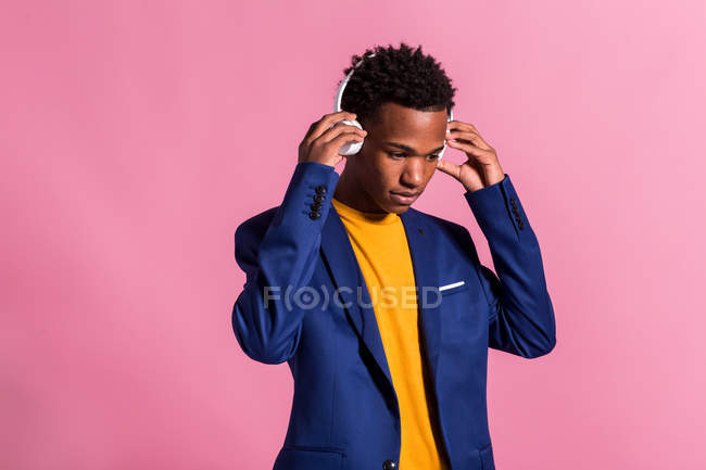 Hombre elegante reflexivo en chaqueta y auriculares sobre fondo rosa - foto de stock