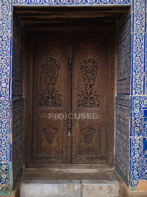 Vue extérieure de la porte sculptée en bois vieilli avec un décor étonnant de tuiles bleues autour, Ouzbékistan — Photo de stock
