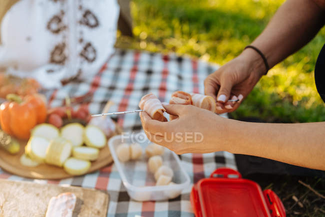 Human hands arranging folded bacon strips on metal skewer for barbecue meal — Stock Photo