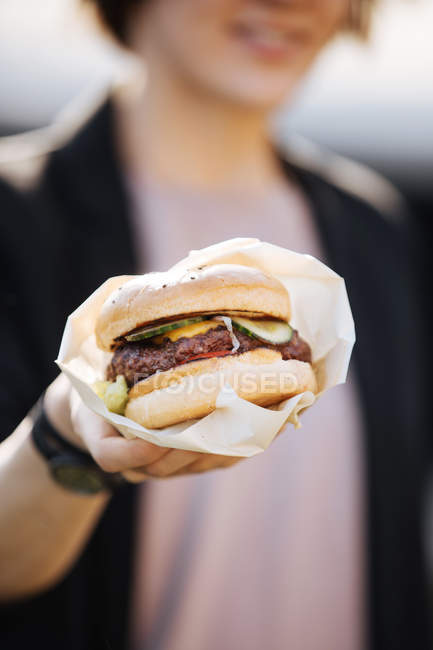 Close-up of female hand holding burger wrapped in paper — Stock Photo