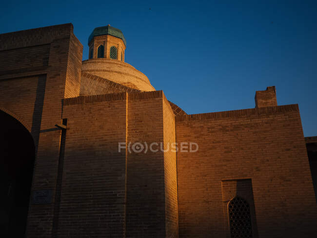 Dal basso colpo di facciata geometrica della moschea di mattoni sotto il cielo blu illuminato con luce dorata del tramonto, Uzbekistan — Foto stock