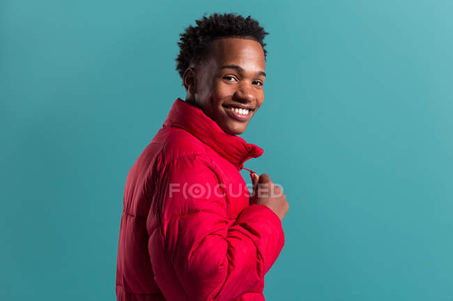 Trendy lächelnder Mann in roter, geschwollener Jacke auf blauem Hintergrund blickt in die Kamera — Stockfoto