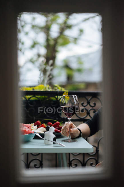 Vue de la récolte de la femelle en chemisier rayé tenant élégant verre de vin blanc assis à la table de planche en bois avec boisson scintillante sur fond flou — Photo de stock