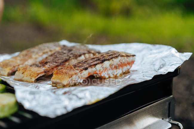 Крупный план сочных кусочков филе лосося на гриле на фольге на открытом воздухе — стоковое фото
