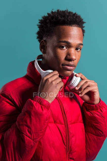 Hombre de moda en chaqueta hinchada roja y auriculares sobre fondo azul - foto de stock