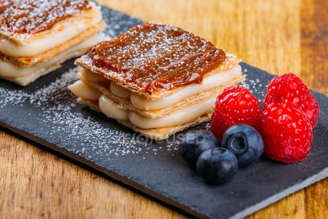 Pastries with cream and caramel topping served on slate with fresh berries — Stock Photo