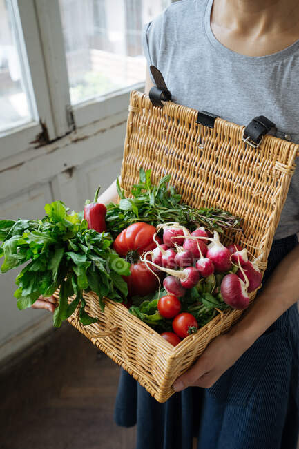 Erntefrau in Hemd und Rock hält in der Hand Korb mit offenem Deckel voller heller frischer Tomaten, Paprika, Rettich und Kartoffeln — Stockfoto