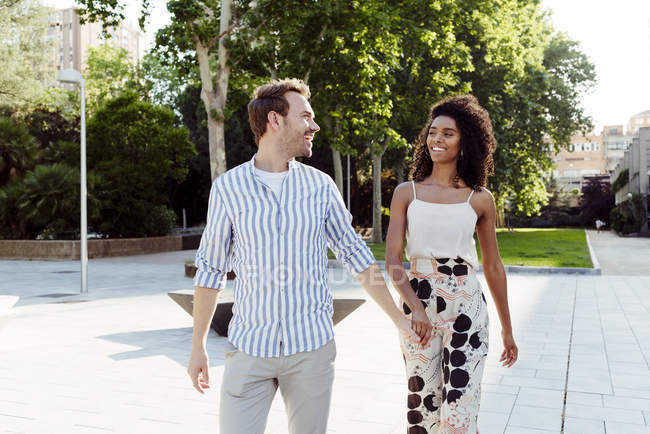 Smiling couple holding hands while walking in city park — Stock Photo