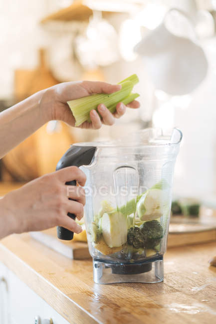Mains féminines mettant céleri dans un bol mélangeur pour smoothie vert — Photo de stock