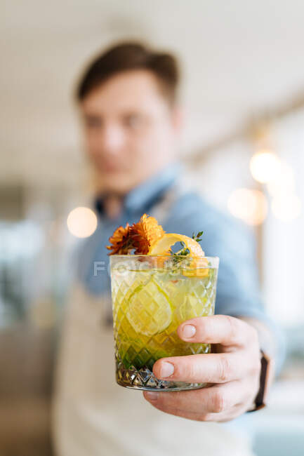 Primo piano di vetro tagliato riempito con cocktail nordico esotico e guarnito con fiori in mano del barista — Foto stock