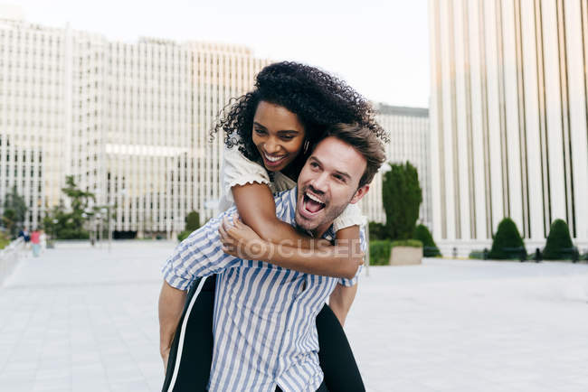 Homem dando passeio de piggyback para mulher afro-americana enquanto se divertindo na rua da cidade juntos — Fotografia de Stock