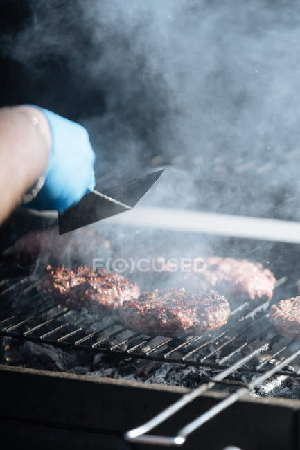 Mains humaines cuisiner des galettes de hamburger crus rôtissant sur grille de barbecue à l'extérieur — Photo de stock