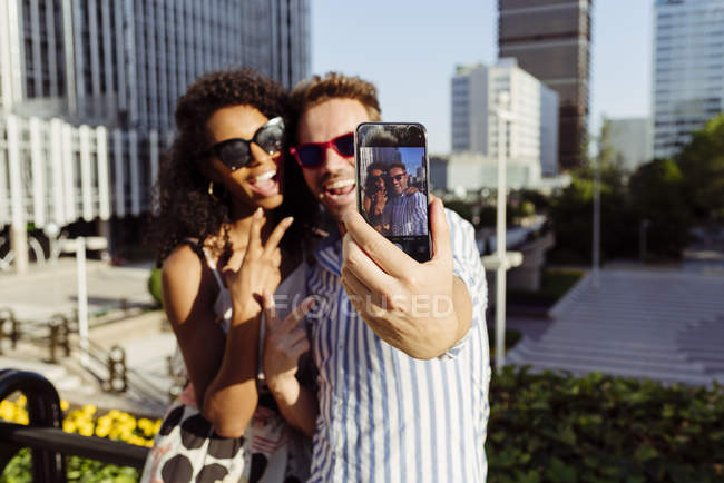 Alegre casal multirracial posando para selfie enquanto em pé no fundo da cidade moderna — Fotografia de Stock