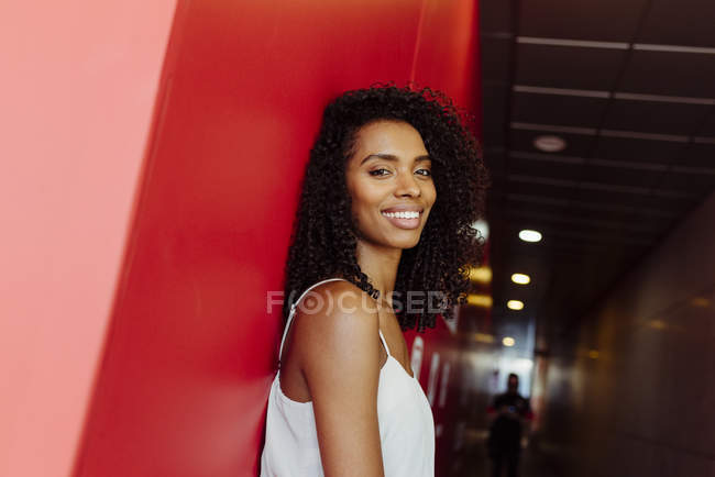 Femme afro-américaine souriante en tenue élégante debout sur fond rouge — Photo de stock
