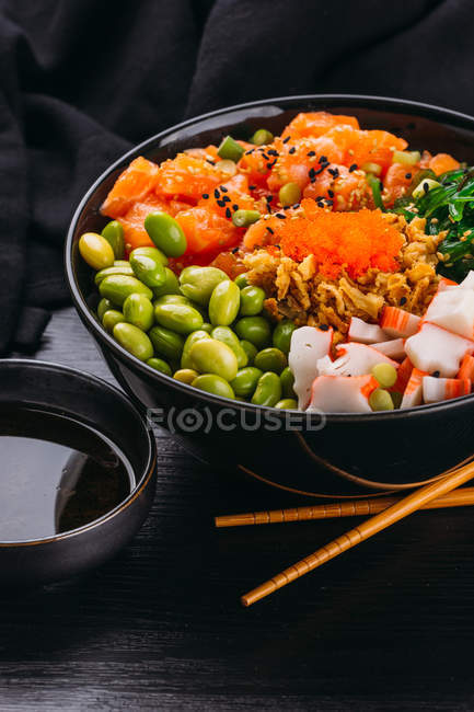Bowl of various Asian food and chopsticks on black wooden tabletop — Stock Photo