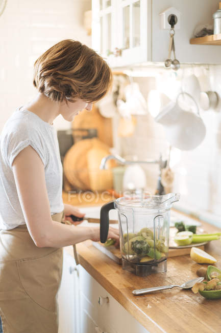 Женщина готовит ингредиенты для приготовления здорового зеленого смузи в блендере — стоковое фото