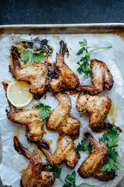 Baking tray with parchment and baked chicken wings in sesame and parsley with lemon — Stock Photo