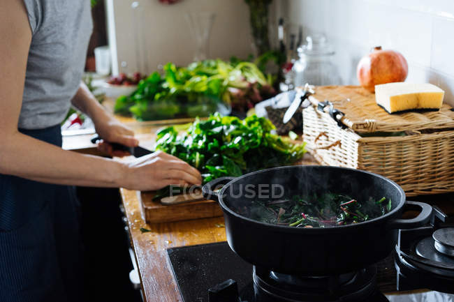 Mulher cortando folhas de espinafre verde na tábua de corte de madeira na mesa — Fotografia de Stock