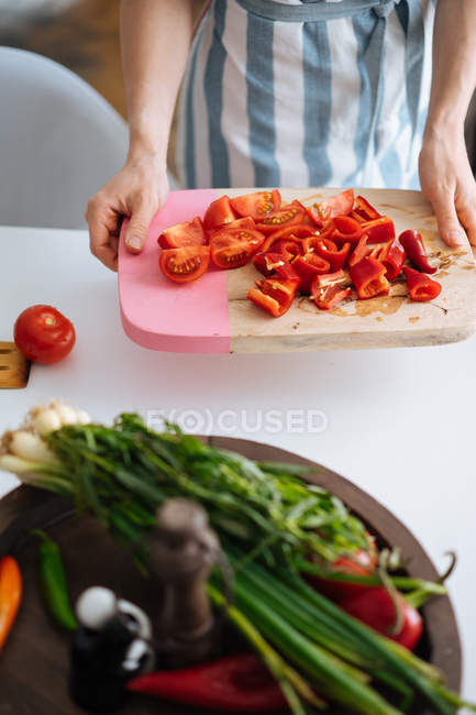 Nahaufnahme weiblicher Hände mit Schneidebrett mit in Scheiben geschnittenen Paprika und Tomaten in der Küche — Stockfoto