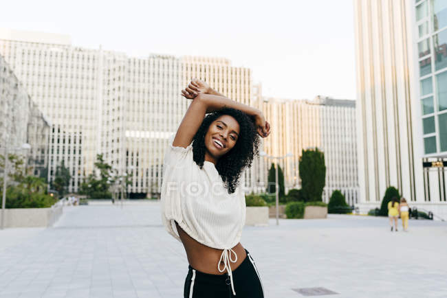 Laughing African-American woman standing on street with hands up and looking at camera — Stock Photo