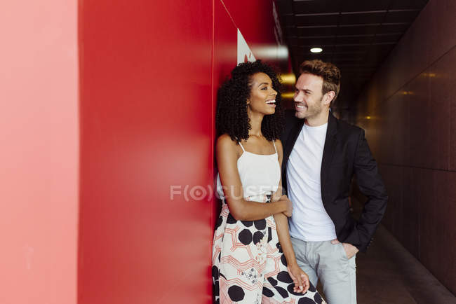 Bonito homem apoiando-se na parede vermelha e flertando com a mulher afro-americana no corredor de construção — Fotografia de Stock