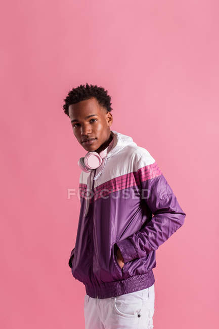 Stylish hipster man in colorful jacket with headphones standing on pink background — Stock Photo