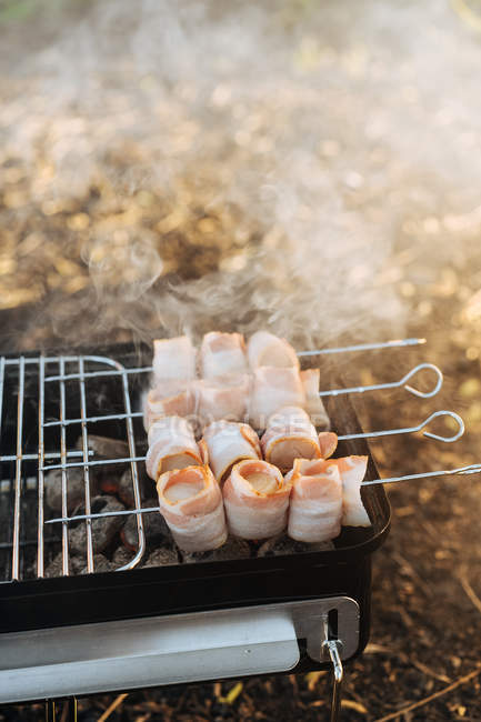 Gros plan de la plaque chauffante portable avec charbon de bois et brochettes avec lanières de bacon grillades — Photo de stock